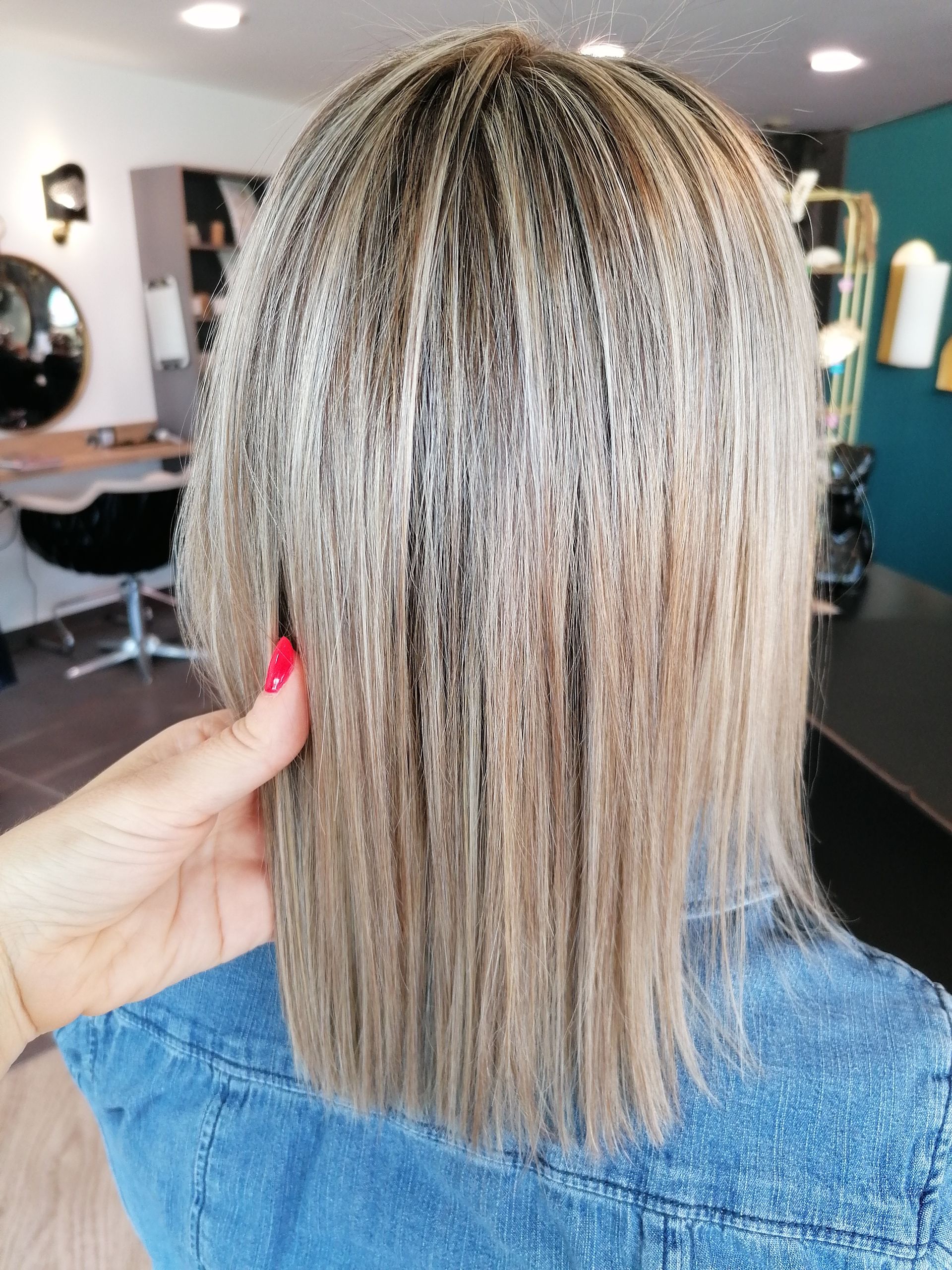 Gros plan sur une coiffure avec le dessus crêpé et les pointes lisses, maintenue par une main dans un salon de coiffure.