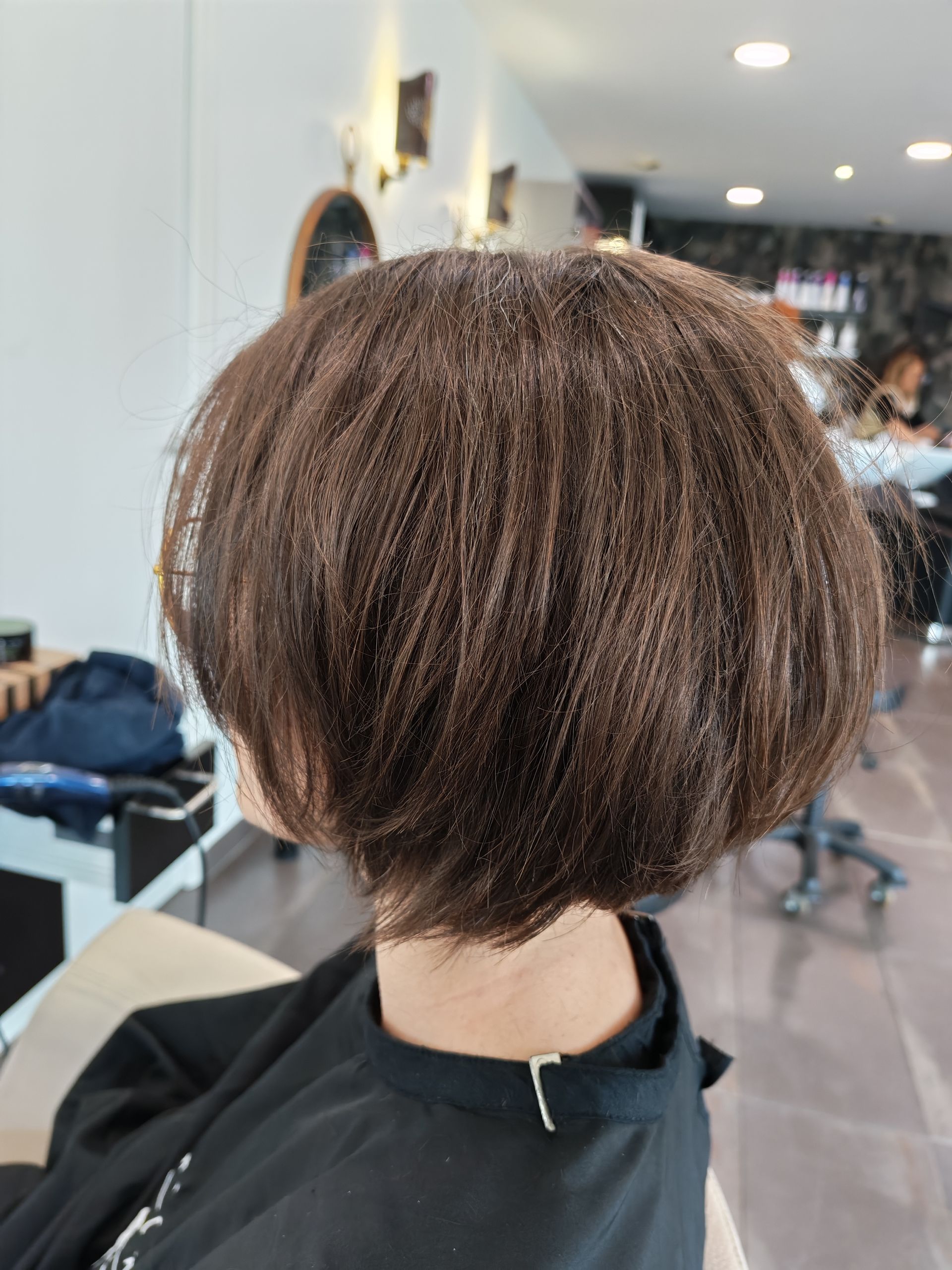 Vue de dos d'une personne avec une coupe au carré courte et brune dans un salon de coiffure.