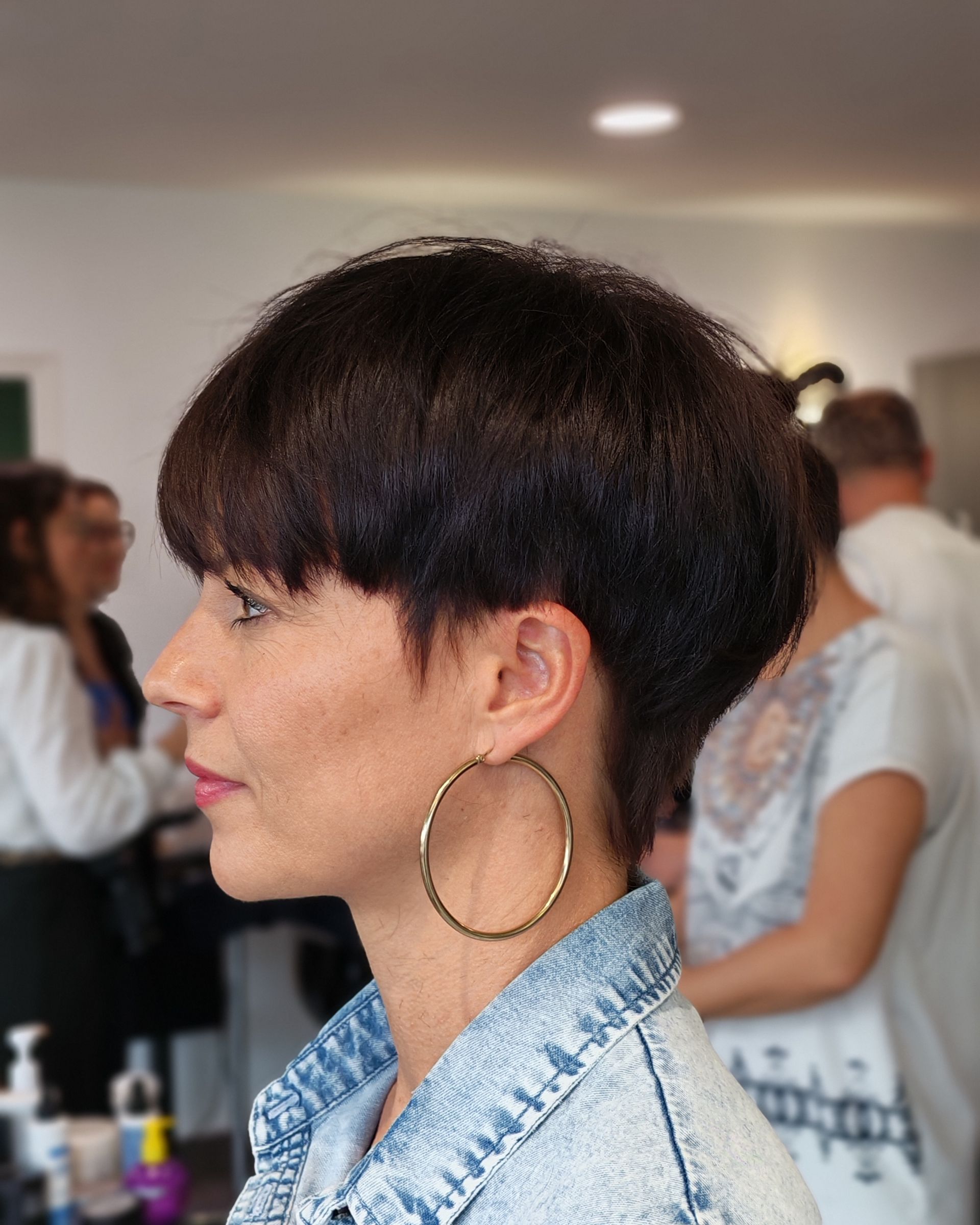 Femme aux cheveux courts et foncés, portant des créoles dorées et une veste en jean.