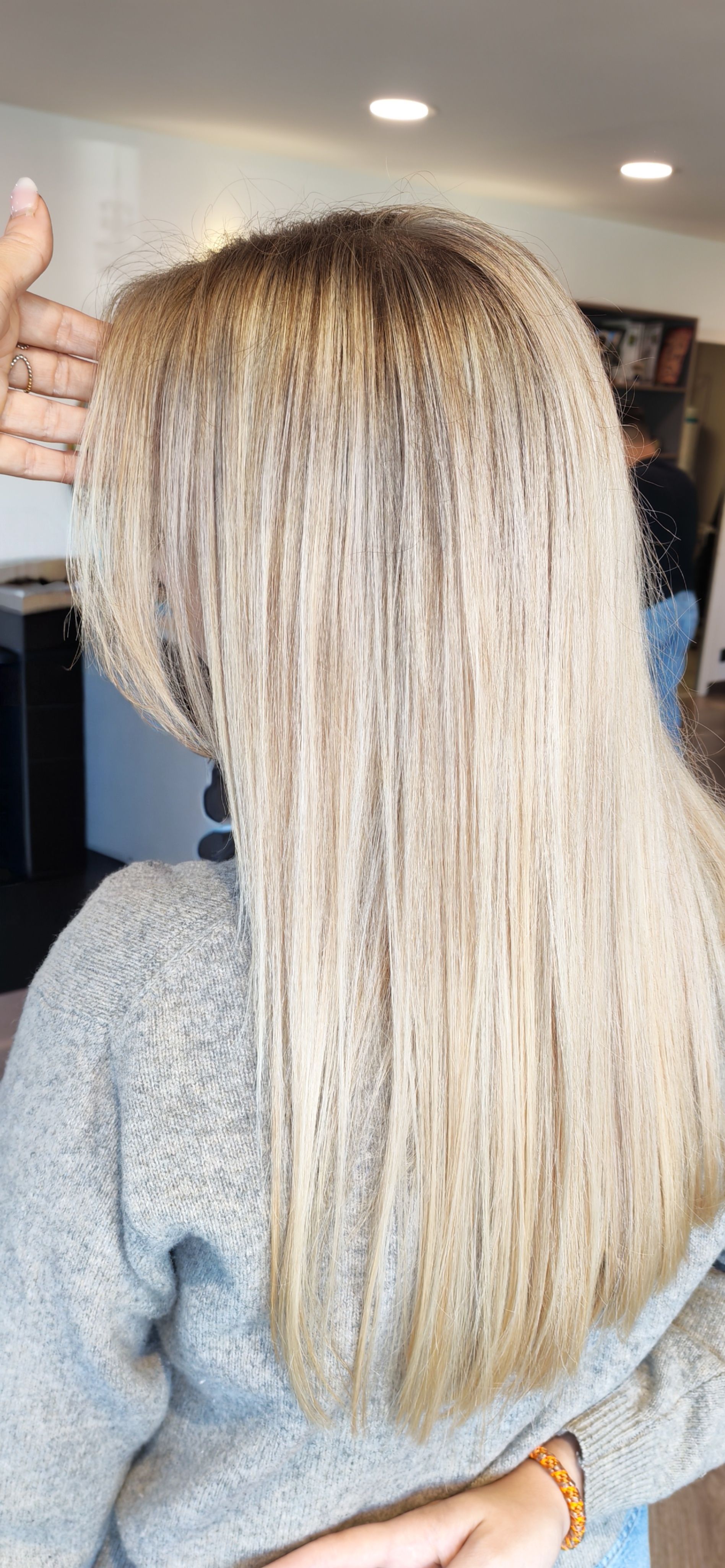 Personne aux cheveux blond clair, vue de dos. La main touche ses cheveux. Elle porte un pull gris.