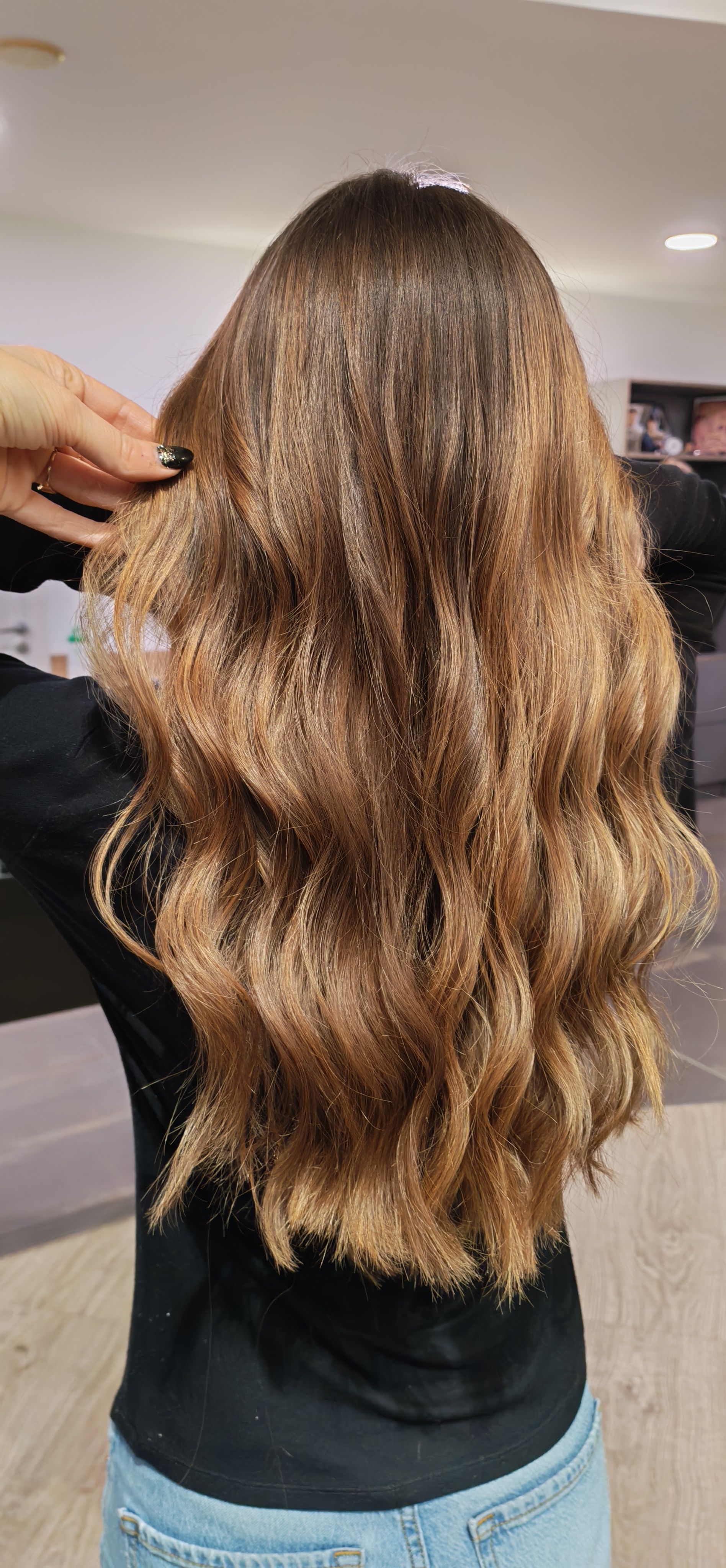 Cheveux longs, bruns et ondulés, tenus en place. Chemise noire, jean bleu, à l'intérieur.