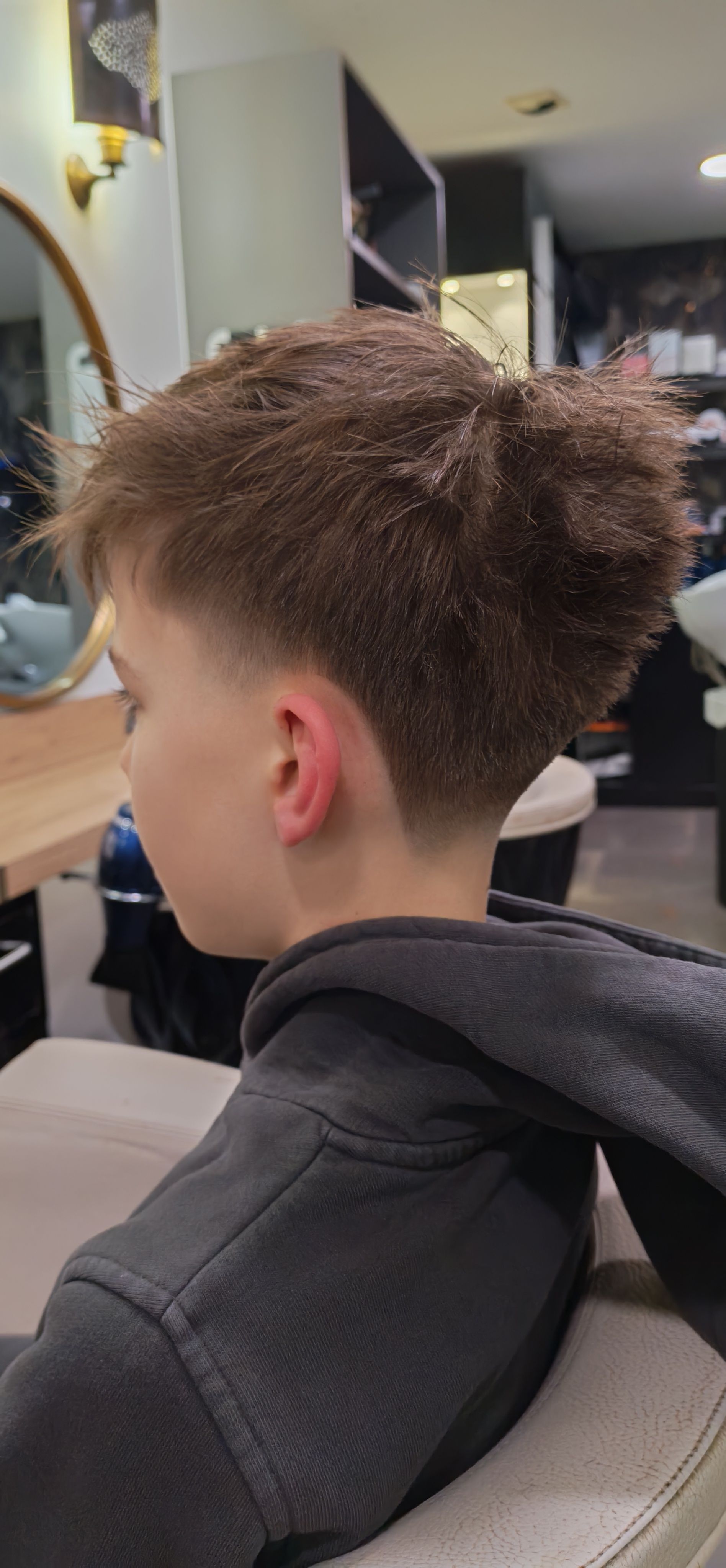 Une personne aux cheveux délavés est assise dans un salon de coiffure. Elle porte un sweat à capuche gris foncé.