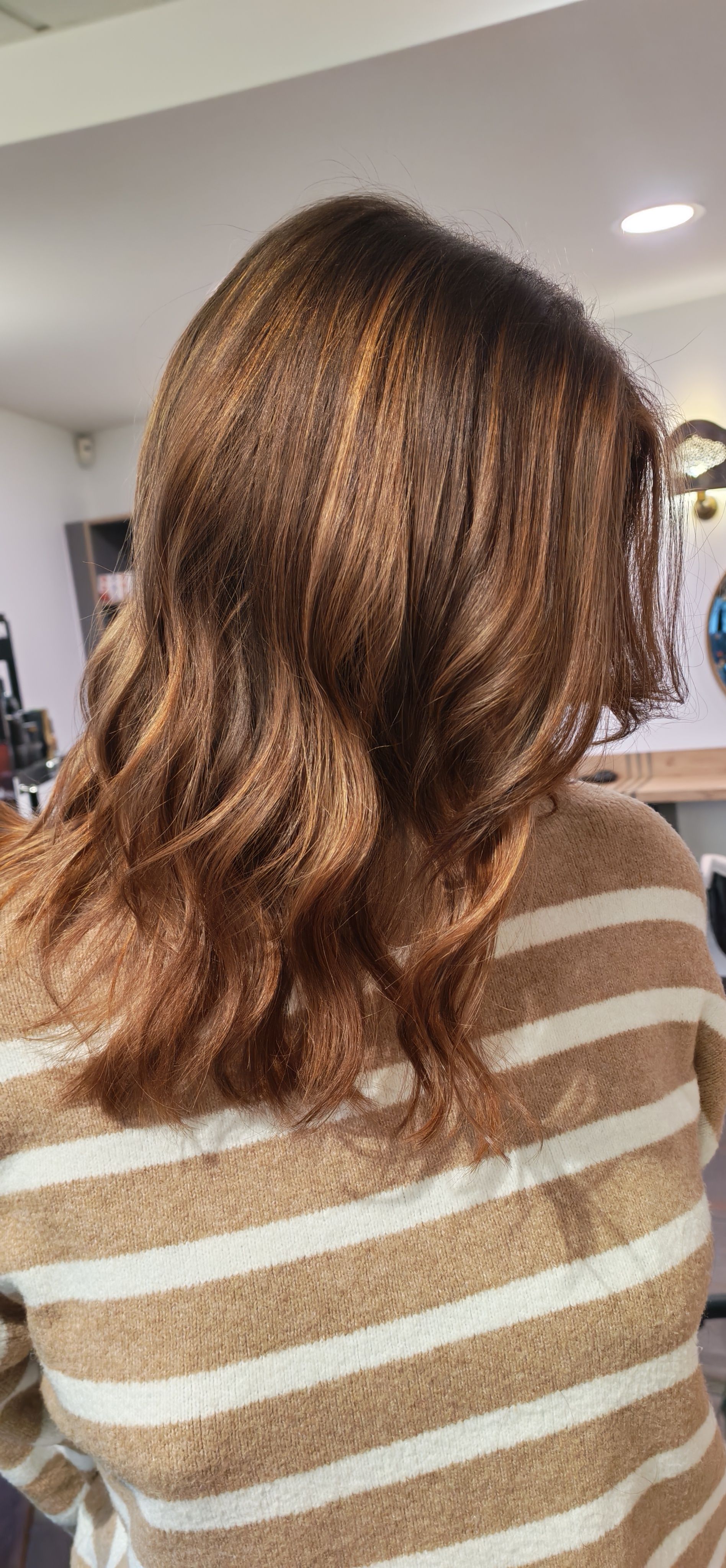 Une personne aux cheveux bruns et bouclés, portant un pull rayé beige, de dos à la caméra.