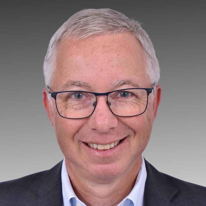Ein Mann mit Brille und Anzug lächelt in die Kamera.