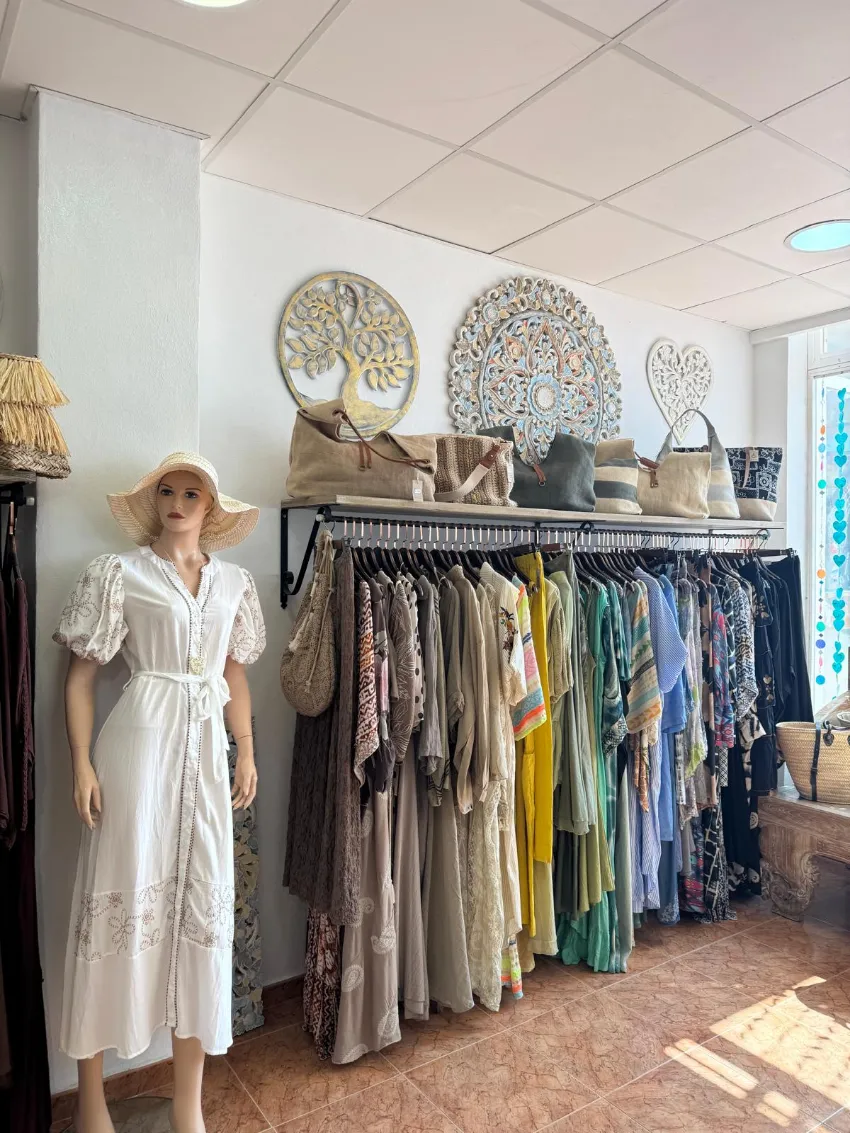 Un perchero de ropa de boutique junto a un maniquí en el interior de una tienda iluminada por el sol.