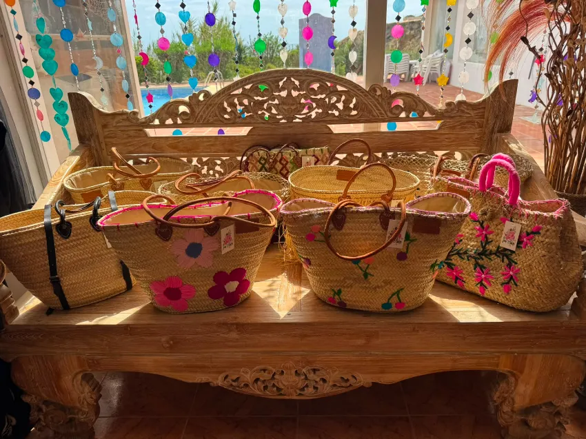 Cestas decorativas de mimbre y pequeños bolsos expuestos en una repisa de madera tallada junto a una ventana.