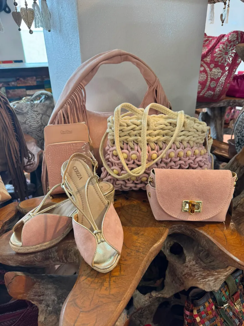 Bolsos y sandalias variados expuestos sobre una mesa de madera en un ambiente de boutique.