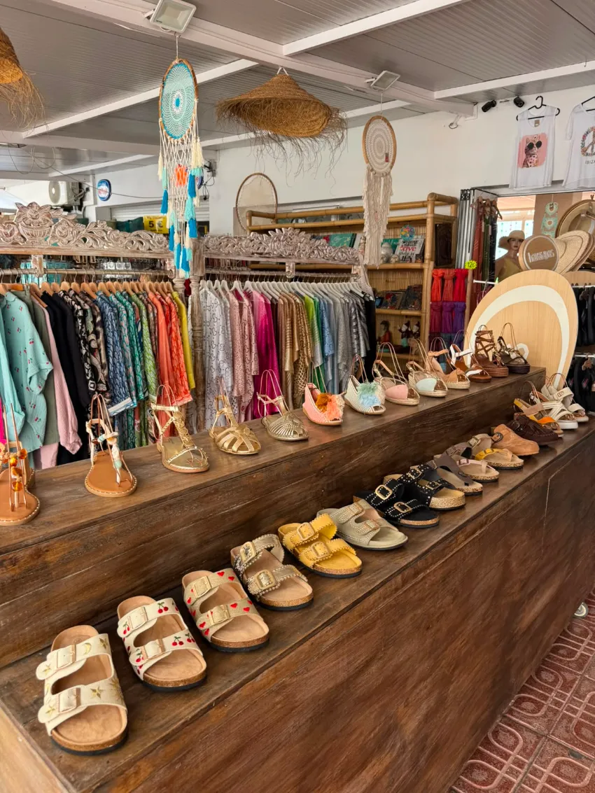 Sandalias y ropa coloridas expuestas en una tienda boutique rústica con estantes de madera.