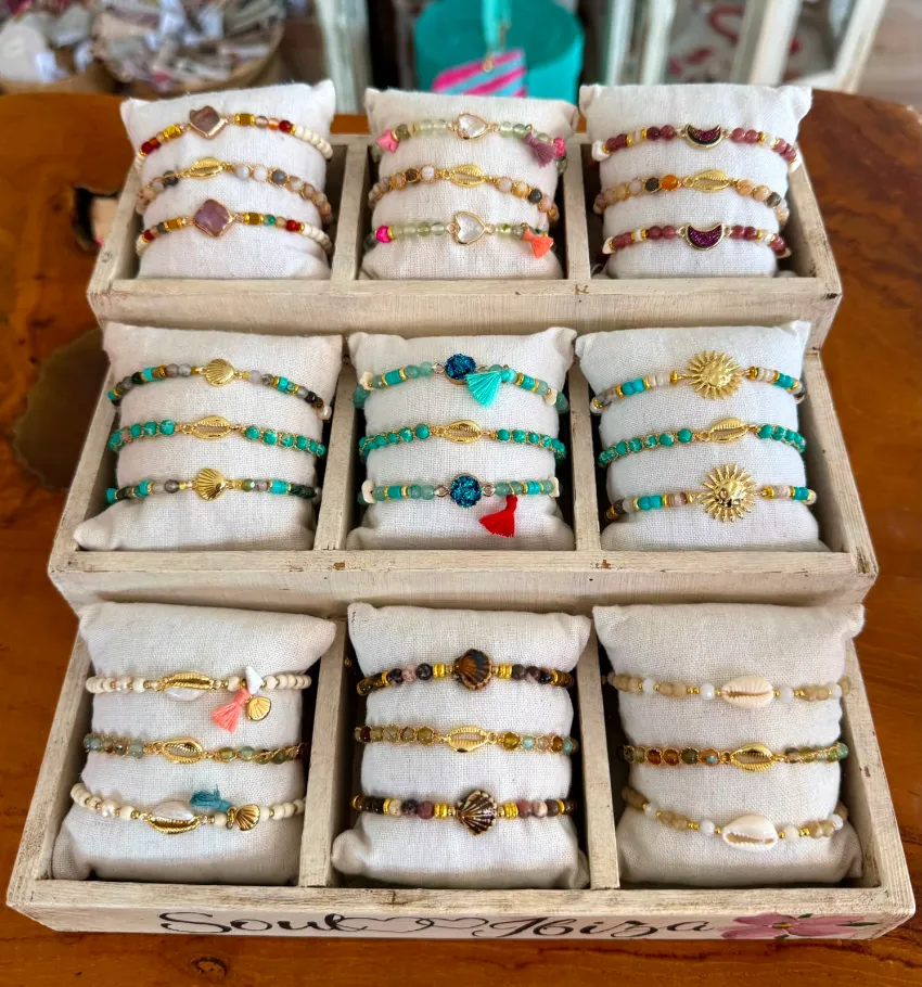 Exhibición de pulseras de cuentas en una bandeja de madera, dispuestas en filas con cojines blancos.