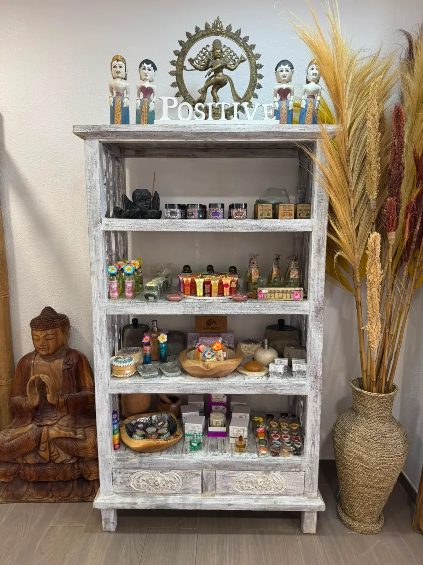 Estantería rústica blanca con tarros y elementos decorativos, flanqueada por una estatua de Buda y hierbas secas en una habitación acogedora.