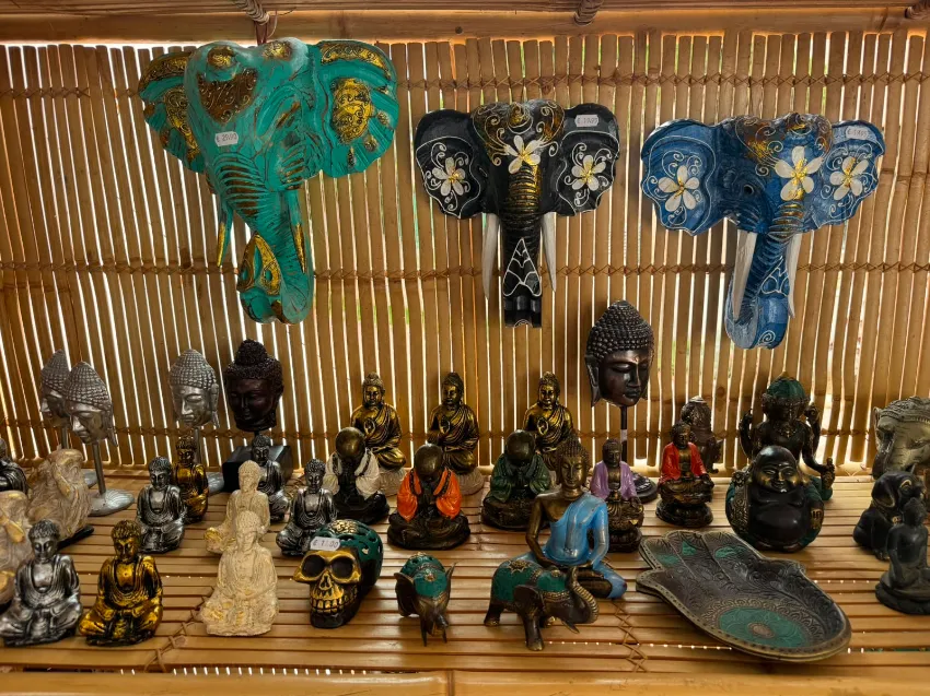 Diversas figuritas y máscaras de elefantes talladas se exhiben en un estante de mercado tejido.