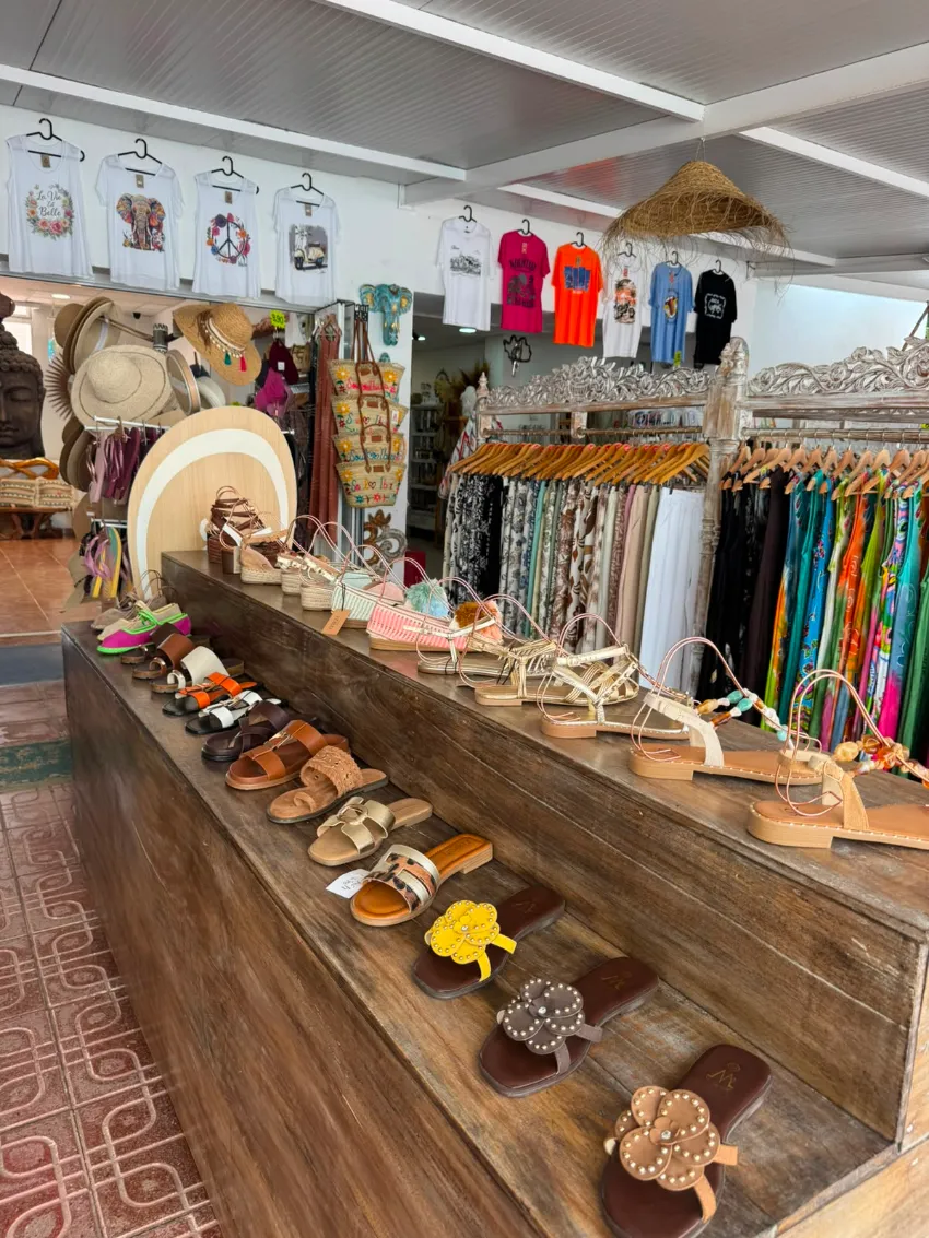 Interior de una pequeña tienda con coloridas prendas colgadas, joyas y accesorios hechos a mano en estantes de madera.