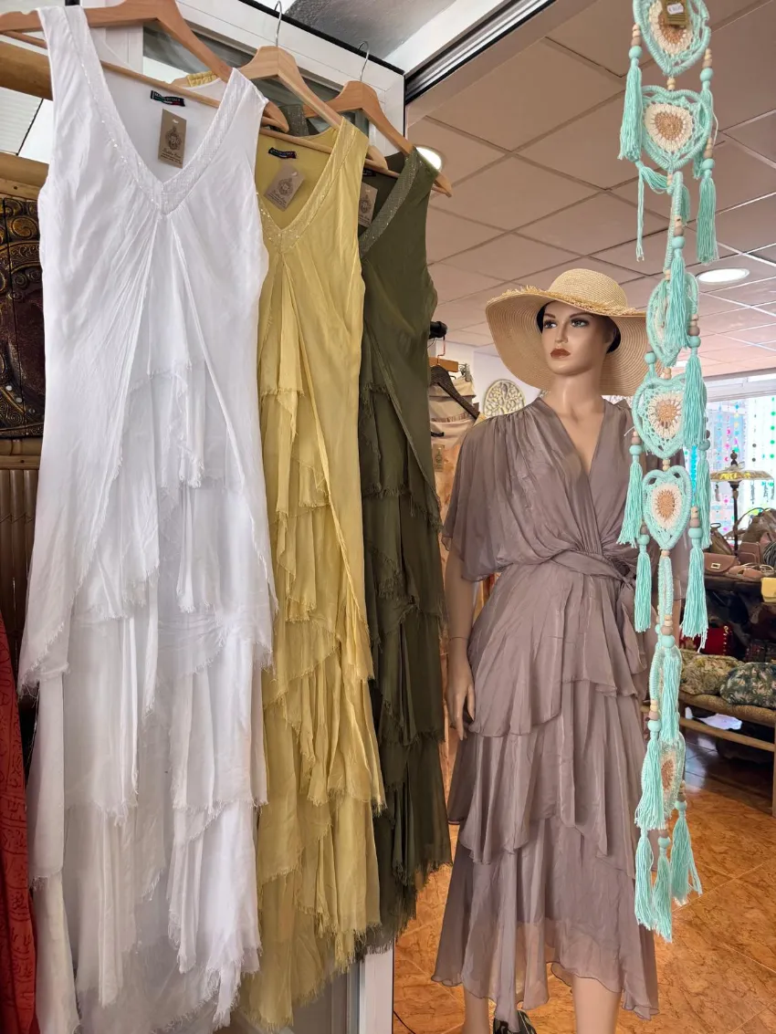 Una mujer con un vestido y un sombrero color topo está mirando vestidos de estilo bohemio colgados en una boutique.