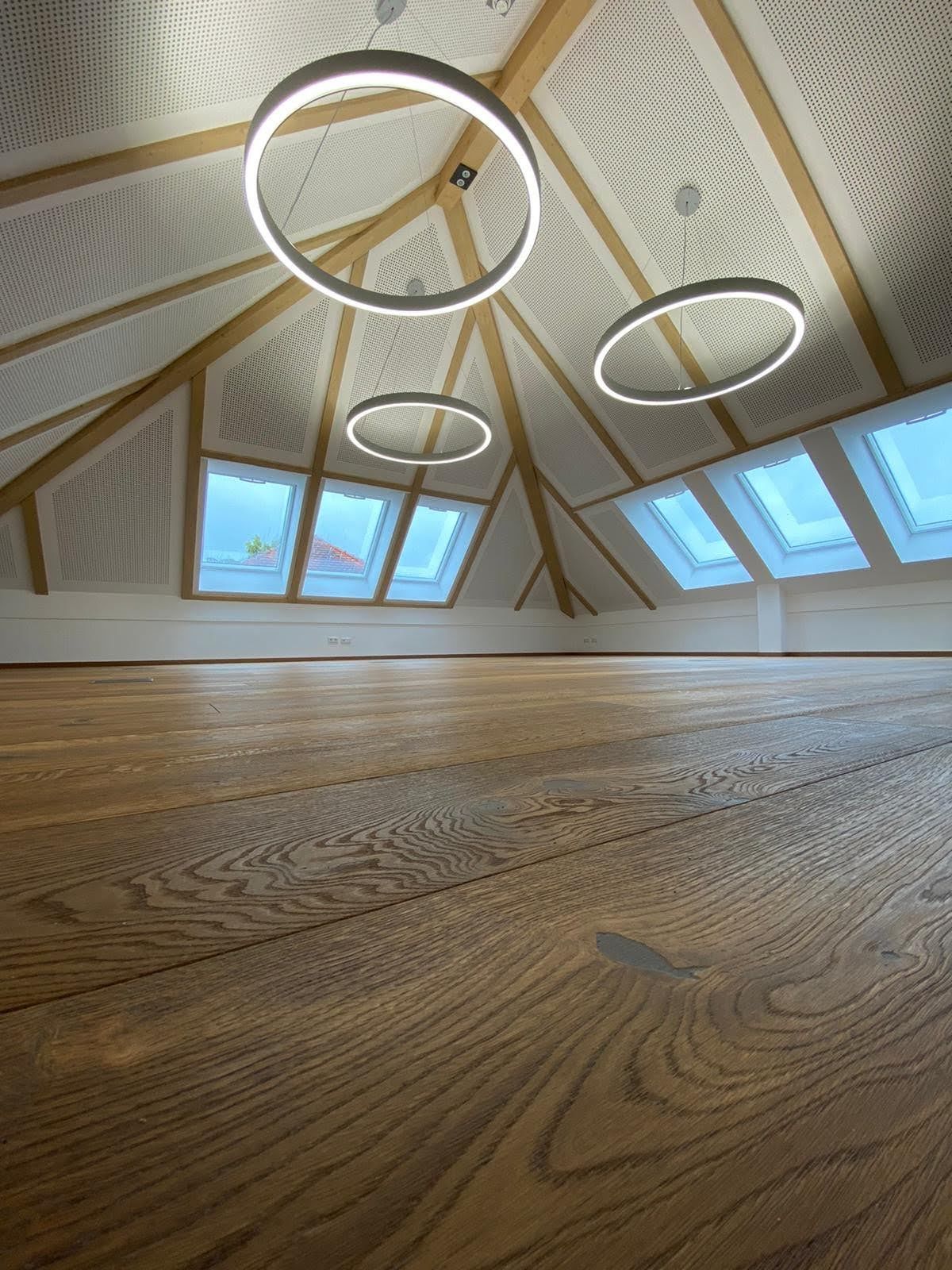 Ein leerer Raum mit einem Holzboden und drei Kronleuchtern an der Decke.