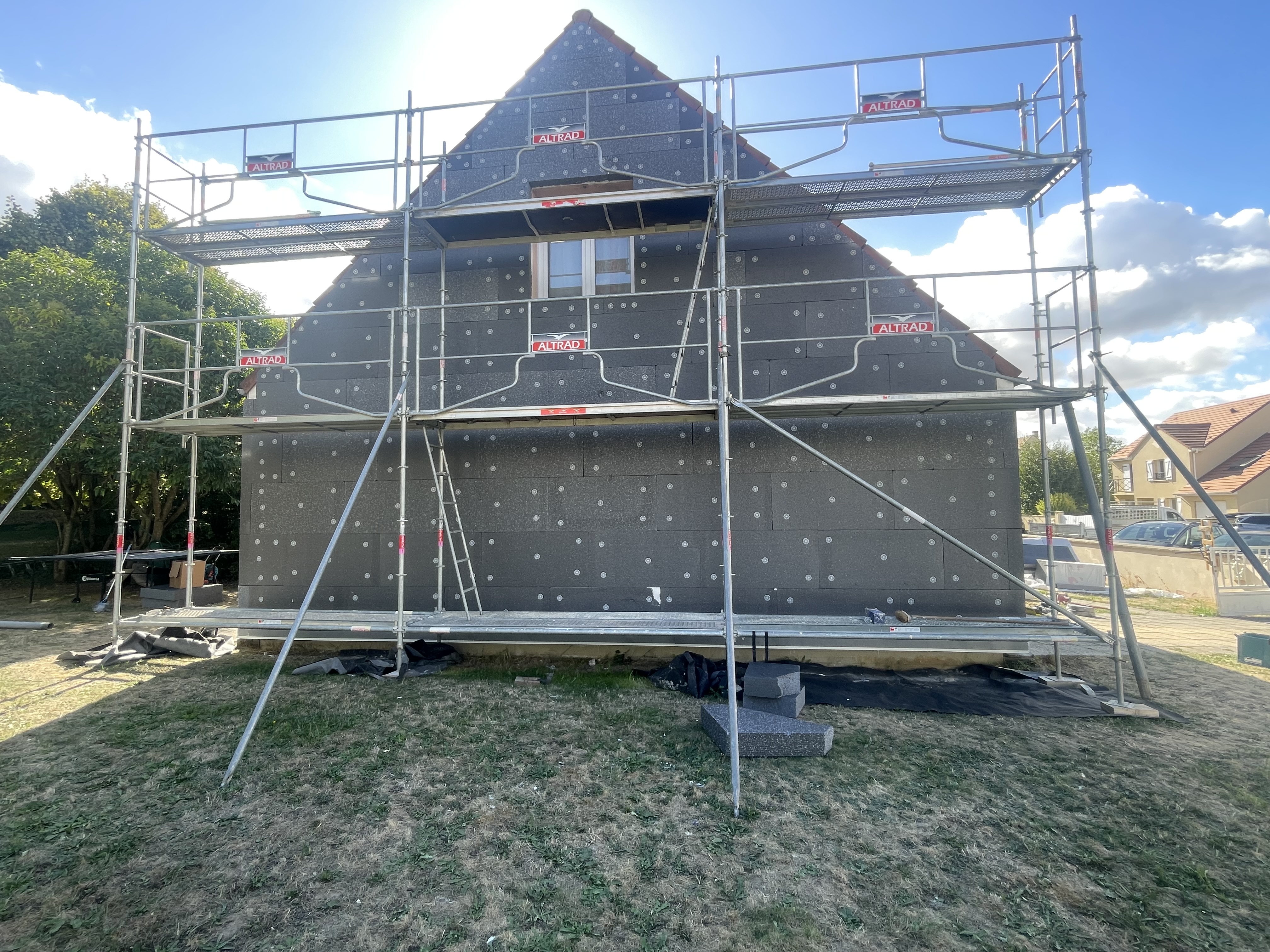 Mur en briques partiellement construit avec échafaudages et panneaux d'isolation gris sur un chantier de construction