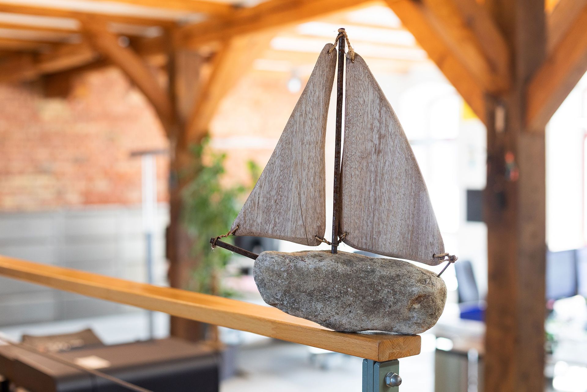 Auf einem Holzgeländer steht ein kleines Modell eines Segelboots.