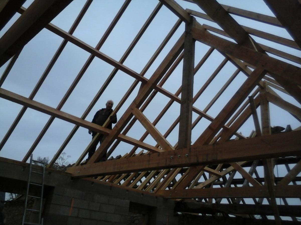 Ossature en bois d'une charpente avec artisan sur le toit