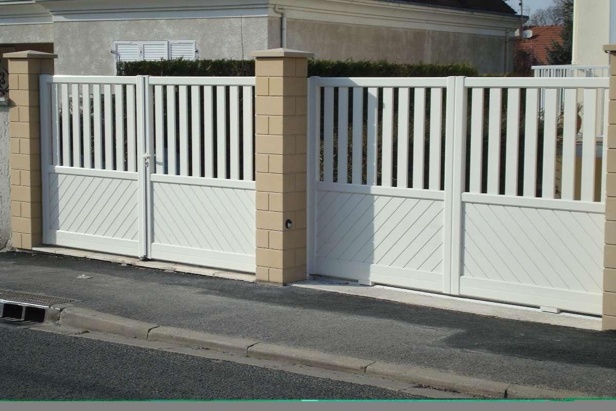 Portail d'allée double blanc avec lattes verticales et panneaux inférieurs diagonaux, placé entre des piliers beiges, sur une allée en asphalte gris.