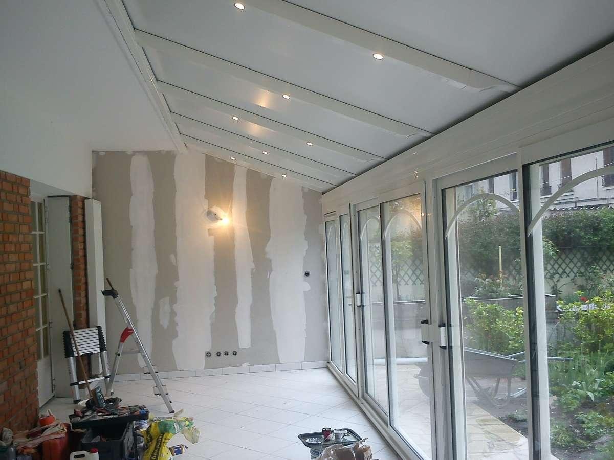 Vue intérieure d'une pièce en construction : murs en plaques de plâtre, portes vitrées et plafond blanc en pente.