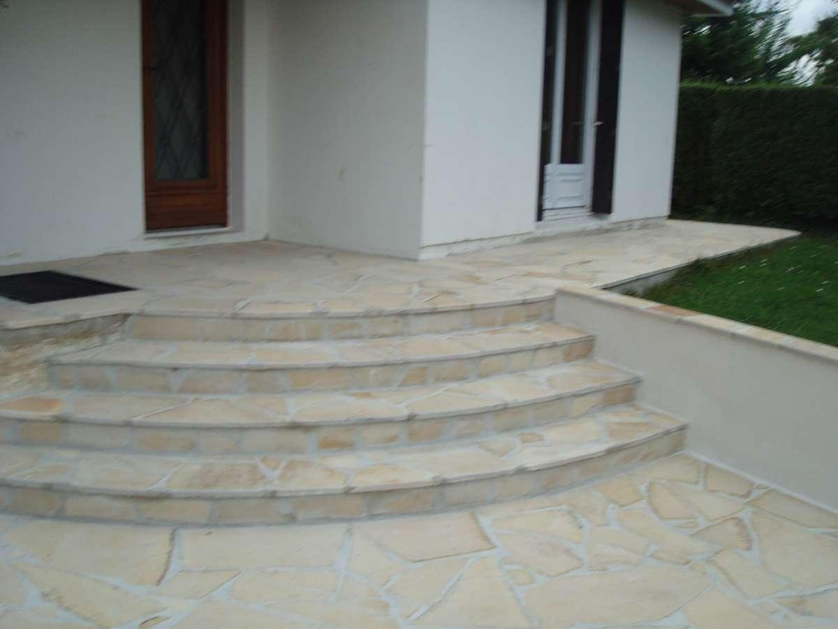 Marches en pierre menant à une entrée de maison avec des murs de couleur claire et une petite pelouse.