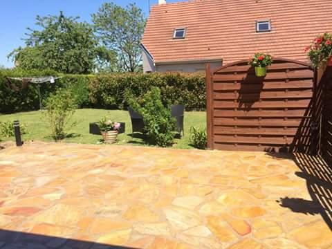 Patio arrière avec dalles brunes, pelouse, clôture en bois et maison.