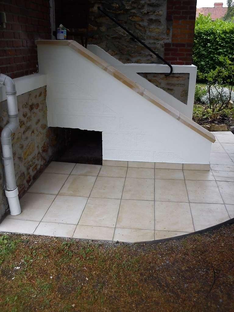Escalier extérieur avec mur peint en blanc et carrelage de couleur claire, menant à une porte.