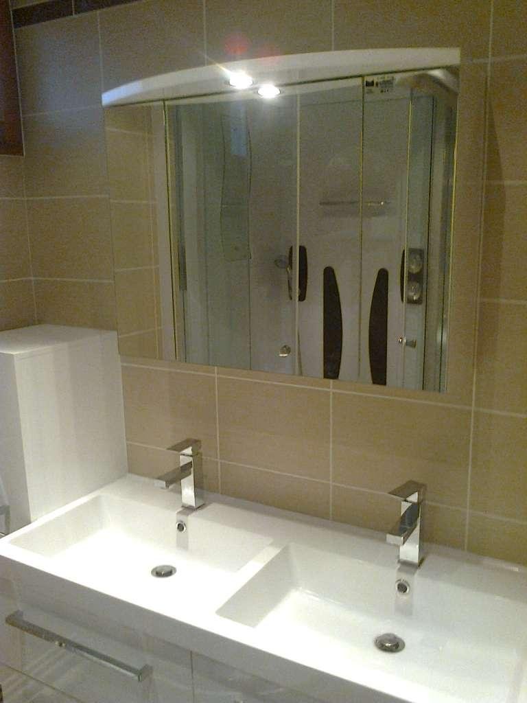 Salle de bain avec double vasque, armoire à pharmacie avec miroir et murs carrelés beiges.