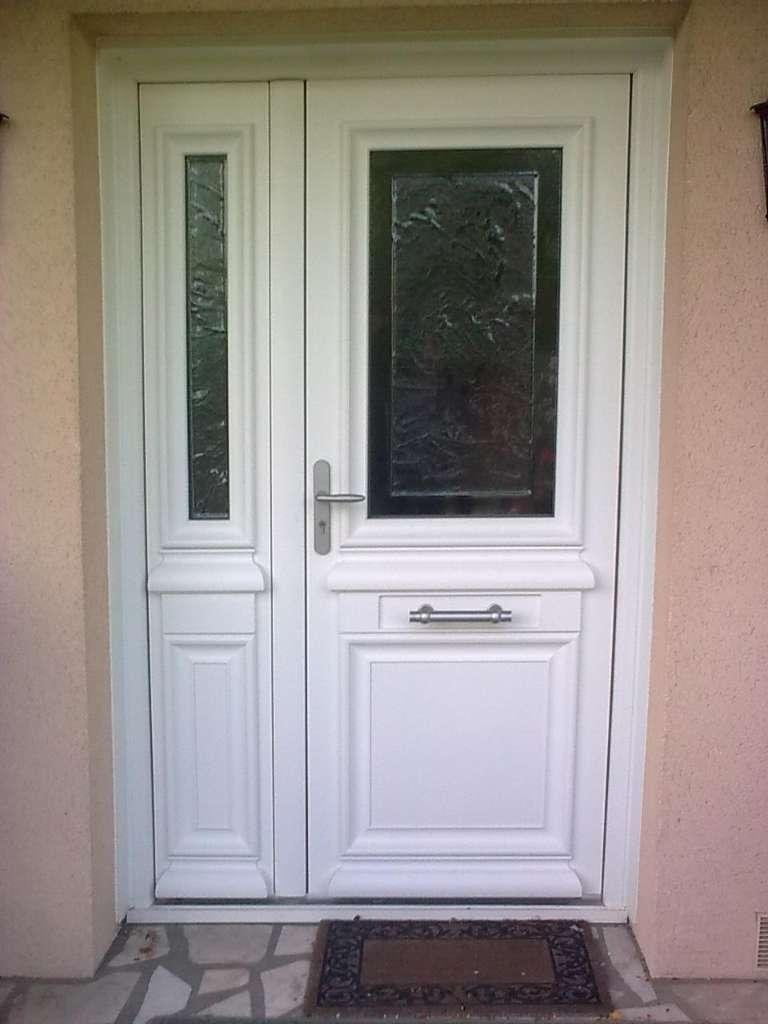 Porte d'entrée blanche avec une fenêtre latérale, encastrée dans un mur extérieur rose clair. Un petit paillasson est placé au bas de la porte.