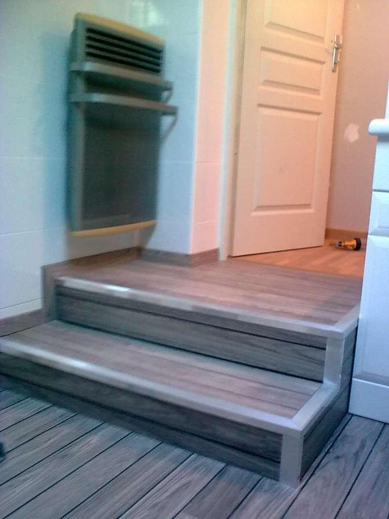 Deux marches en bois avec des garnitures argentées à côté d'une porte, un radiateur mural est fixé au mur.