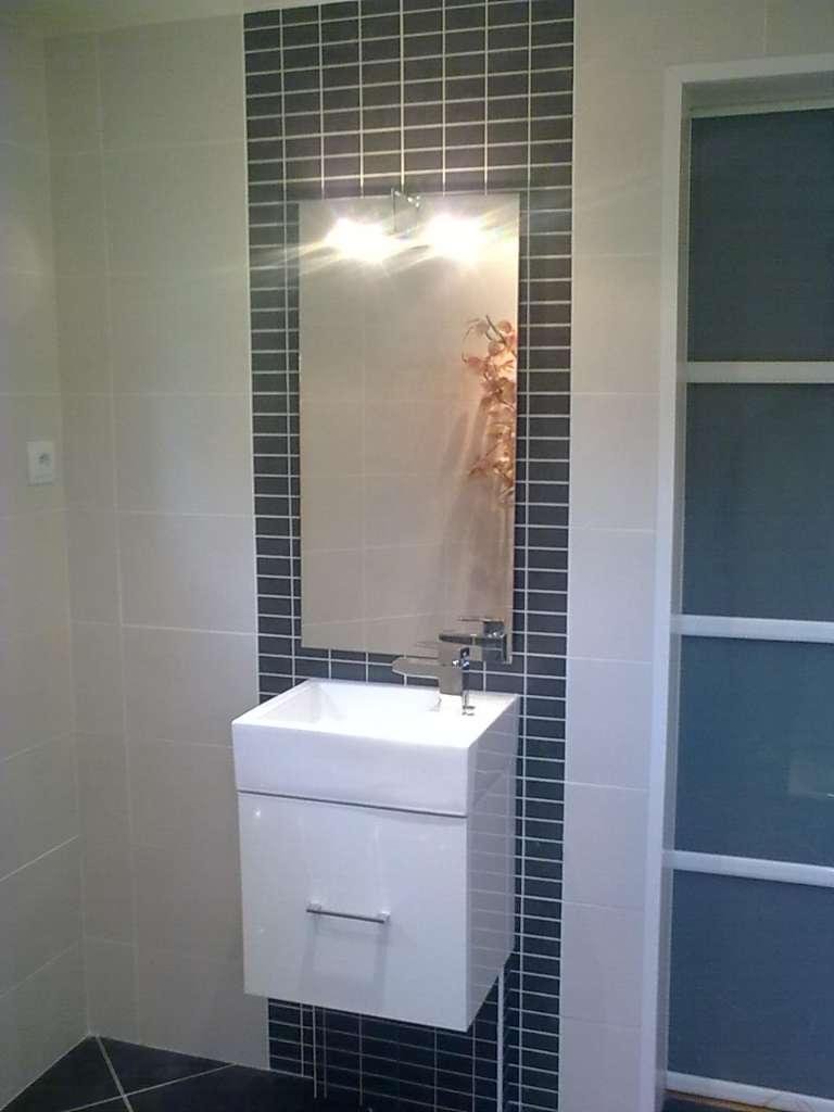 Lavabo de salle de bain mural blanc avec miroir encadré de carreaux de mosaïque noirs.