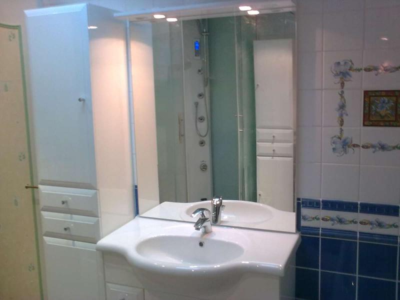 Salle de bain avec armoires blanches, lavabo, grand miroir et murs carrelés bleus et blancs.