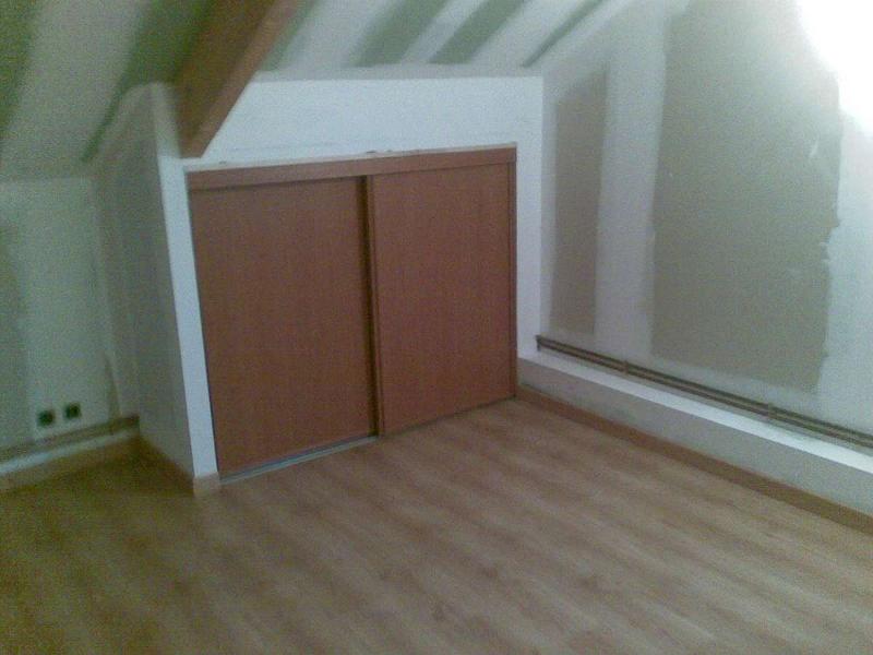 Chambre mansardée avec parquet imitation bois, placard intégré avec portes coulissantes marron, cloisons sèches et lumière.