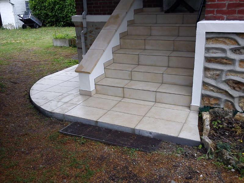 Escalier en pierre menant à l'entrée d'une maison, avec un palier incurvé et un carrelage beige.