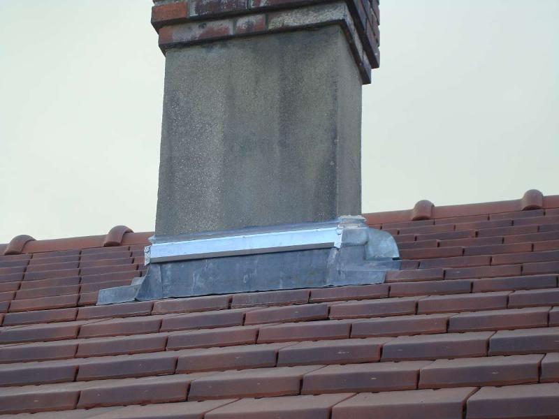 Cheminée sur un toit en tuiles de terre cuite, avec solin métallique autour de sa base.