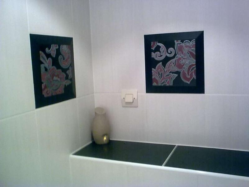 Coin salle de bain avec inserts en carrelage floral, étagère noire et prise murale.