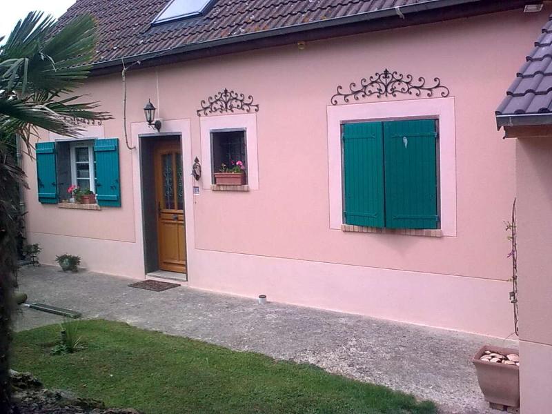 Maison rose avec volets verts et ferronnerie décorative ; pelouse verte devant.