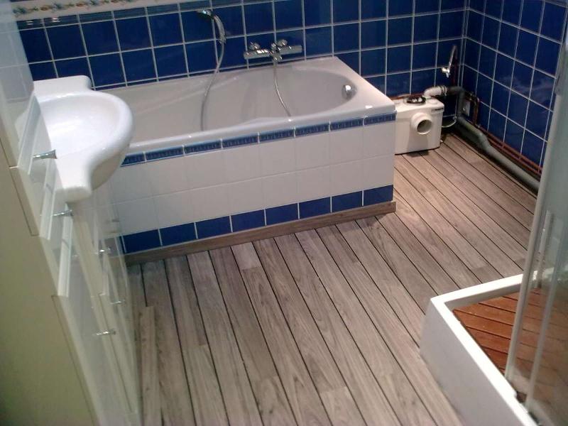 Salle de bain avec carrelage bleu, baignoire blanche et sol imitation bois clair.