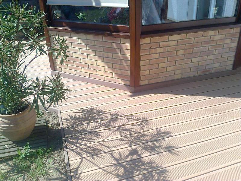 Mur de briques et terrasse marron avec une plante en pot projetant une ombre lors d'une journée ensoleillée.