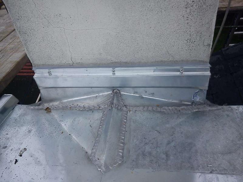 Joint de conduit métallique soudé à une structure en béton, fixé avec des vis, à l'extérieur.