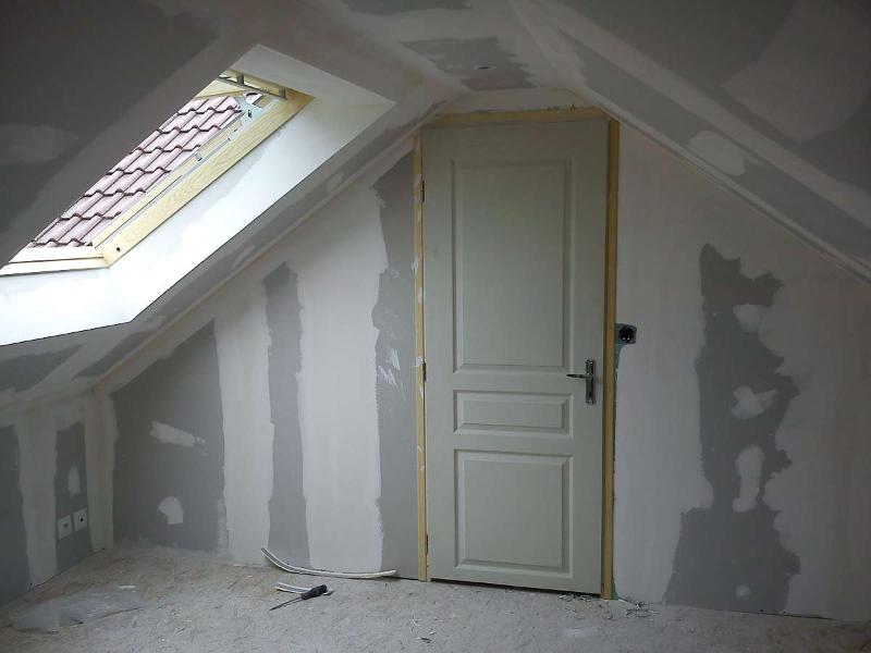 Grenier avec porte, puits de lumière et cloisons sèches. Murs gris clair ; porte blanc cassé.