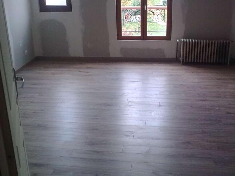 Chambre avec nouveau parquet aspect bois; murs nus avec fenêtre et radiateur; palette de couleurs neutres.