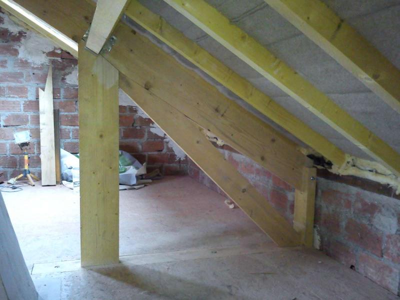 Poutres de support en bois dans un grenier, construites contre des murs en briques.