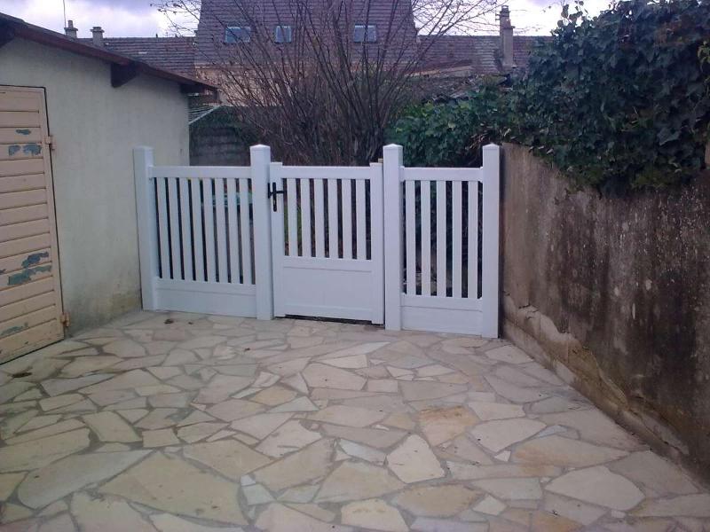 Portail en bois blanc dans une cour pavée, menant à un quartier résidentiel.