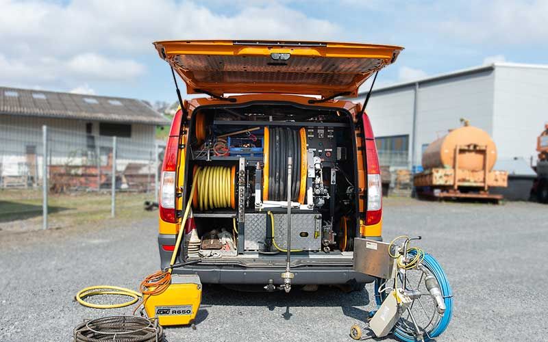 Auf einem Parkplatz steht ein gelber Lieferwagen mit einem Haufen Werkzeug auf der Ladefläche.