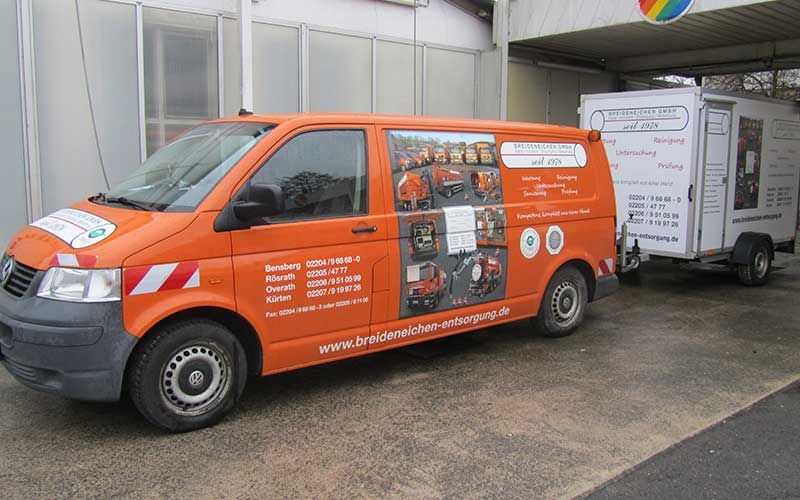 Ein orangefarbener Lieferwagen mit Anhänger steht vor einem Gebäude.