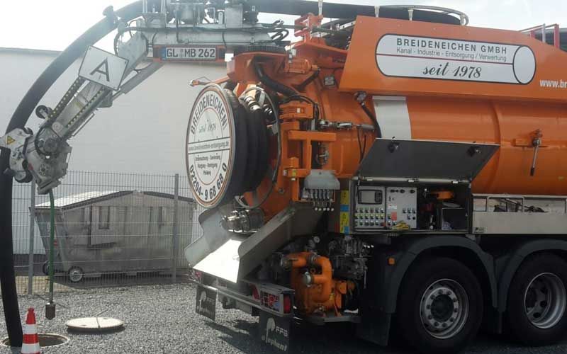 Auf einem Parkplatz steht ein großer orangefarbener Saugwagen.