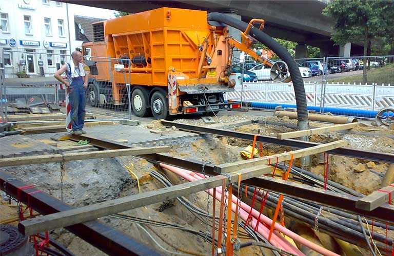 Ein Mann steht auf einer Baustelle neben einem großen orangefarbenen Lastwagen.