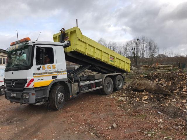 Camion-benne blanc et jaune chargé de débris sur un chantier 