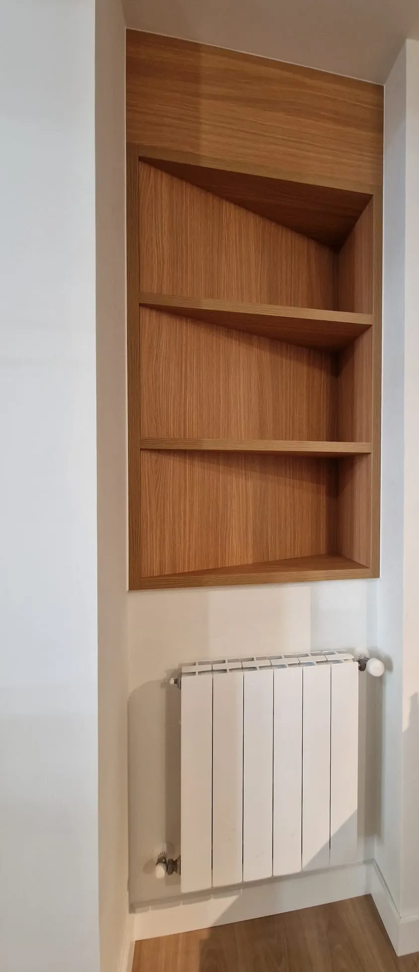 Una habitación con un estante de madera y un radiador blanco.
