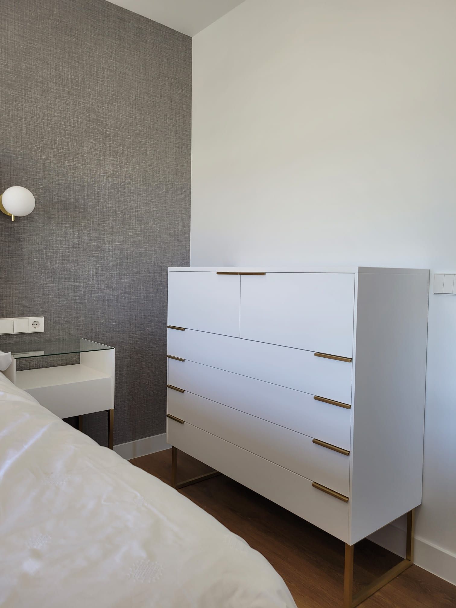 Hay una cómoda blanca en un dormitorio al lado de una cama.